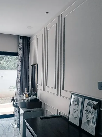 A view of a completed Gurgaon residence bedroom, showing the finished wall molding and a dedicated vanity area. The design focuses on creating a soothing atmosphere with a clean, monochromatic color scheme.