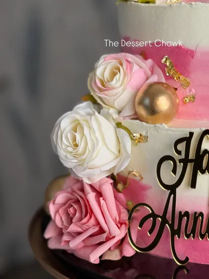 A detail shot of the fresh roses and gold leaf accents that add a touch of luxury to this anniversary cake.