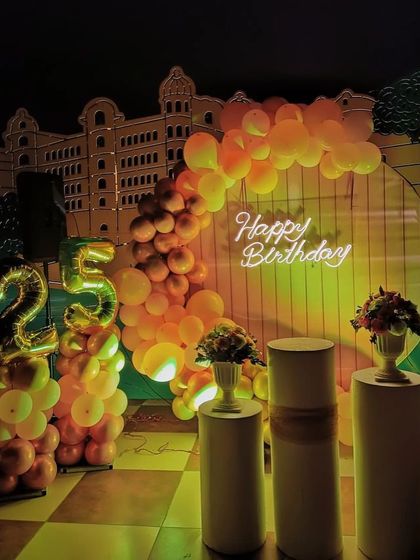 This 25th birthday setup uses a warm, sunset-inspired color palette of orange and yellow balloons. The "Happy Birthday" neon sign and marquee '25' create a glowing, cheerful atmosphere.