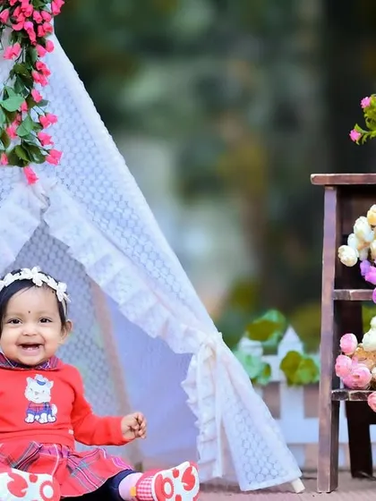 A happy baby girl in a red outfit playing in a floral teepee setup.