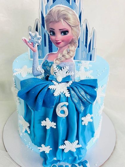 A beautiful Frozen cake featuring Elsa in her iconic blue dress, made of fondant, with an ice castle in the background.