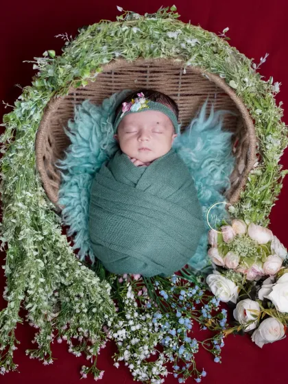 This sleeping newborn is nestled in a basket adorned with greenery, creating a natural and organic feel for this beautiful portrait.