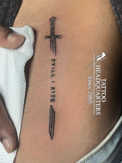 A broken sword tattoo with the words "STILL I RISE" in the middle, symbolizing resilience and strength through hardship.
