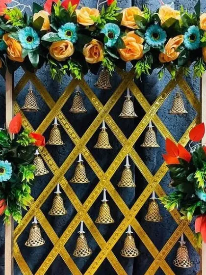 For a touch of traditional artistry, I designed this unique backdrop using a golden jaali or lattice frame. Each opening is decorated with a delicate golden bell, and the frame is topped with a colorful arrangement of artificial flowers.