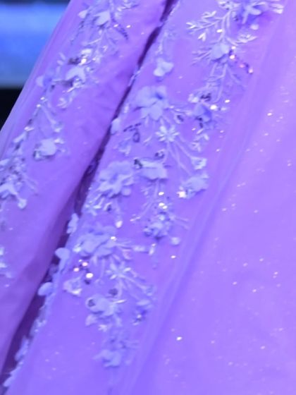 A macro view of the hand-sewn 3D flowers and glittering sequins on the lavender tulle, showcasing the hours of artistry in each gown.