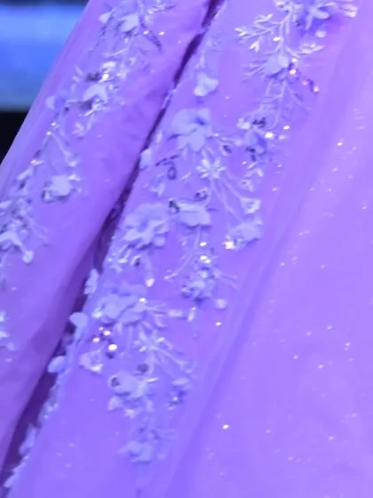 A macro view of the hand-sewn 3D flowers and glittering sequins on the lavender tulle, showcasing the hours of artistry in each gown.