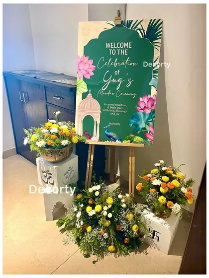 A custom welcome sign for a Mundan ceremony, designed with traditional Indian motifs like lotuses and peacocks. The entrance is decorated with fresh floral arrangements to greet guests.