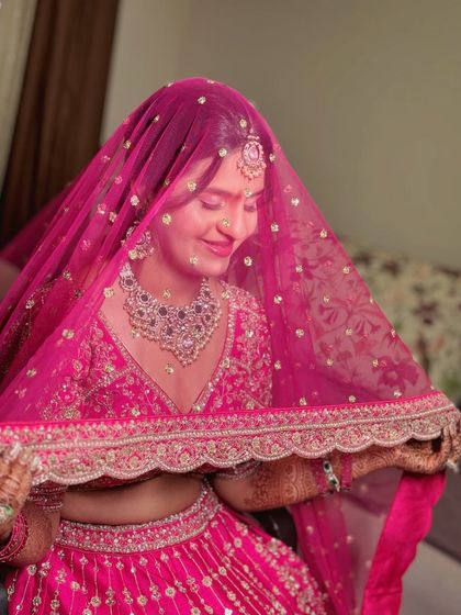 A classic bridal pose with the veil. The sheer pink dupatta creates a soft, dreamy effect, highlighting her smile and beautiful makeup.