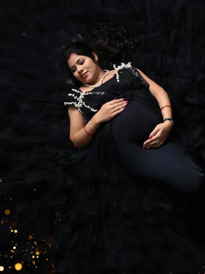 An artistic overhead shot with a dramatic flair. The mom-to-be lies on a bed of black tulle, with golden sparkles adding a touch of magic to the dark, moody theme.