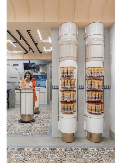 We reimagined the traditional column as a multi-functional design element. Here, it is split to create both a standing table and a vertical display unit for snacks, topped with a light fixture covered in natural banana fiber.