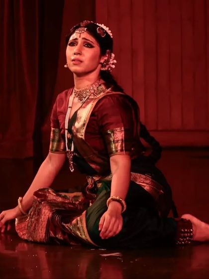 A poignant moment of 'abhinaya', where the character is lost in thought or sorrow. The red lighting enhances the emotional intensity of the scene.