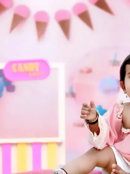 A sweet baby girl in a pink dress enjoys a treat in our vibrant candy shop themed set, perfect for a fun birthday shoot.