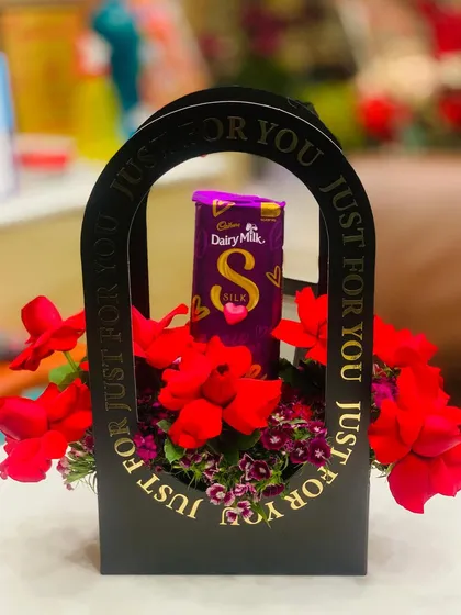 A simple yet elegant gift box arrangement. This black "Just For You" carrier holds a Cadbury Silk chocolate bar surrounded by artificial red flowers.