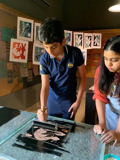Two students work together at the inking station, preparing a plate for the printing press.