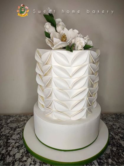 Another view of the modern two-tiered wedding cake with its intricate folded fondant texture. This design requires precision and patience, but the result is a unique and stunning architectural look.