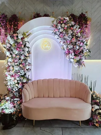 The main stage for a floral-themed baby shower. The layered arch backdrop is framed by a cascade of fresh flowers in shades of pink and purple, creating a stunning focal point.