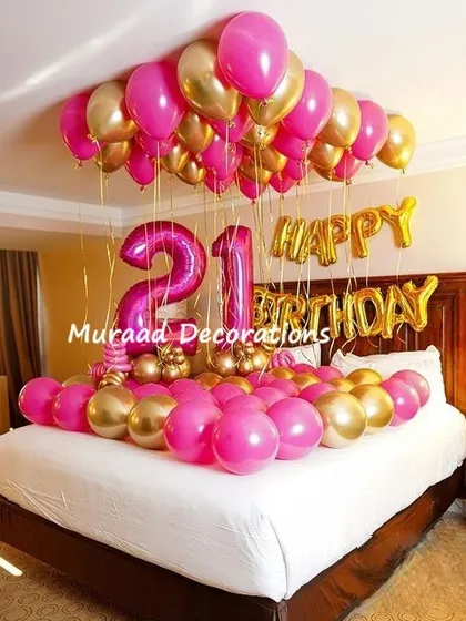 A chic pink and gold bedroom decoration for a 21st birthday. The bed is filled with balloons, and more balloons with long ribbons float on the ceiling, creating a very festive and celebratory feel.