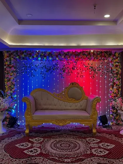A simple yet impactful stage design with a fairy light backdrop, a classic diwan, and dramatic red and blue uplighting for a vibrant look.