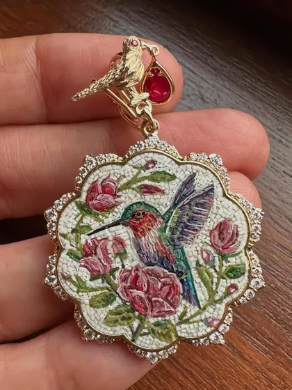 A detailed, in-hand view of the hummingbird and roses pendant. You can see the individual mosaic pieces that form the image, a testament to this meditative craft.