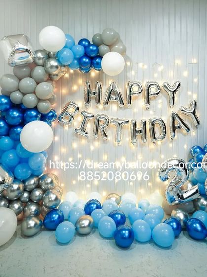 A stylish blue, silver, and white birthday decoration. This setup includes a balloon garland, 'Happy Birthday' foil letters, and fairy lights for a modern and celebratory look.