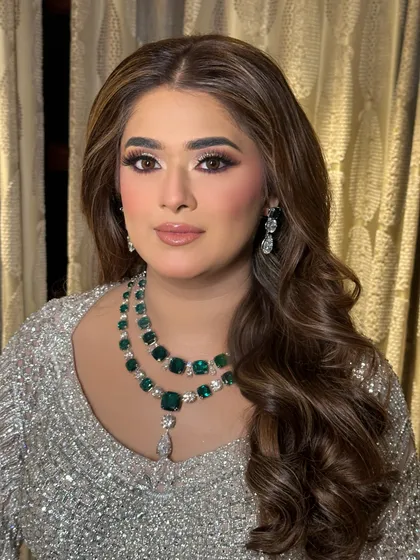 A close-up of a glamorous reception look. The makeup features a soft smokey eye and beautiful Hollywood waves, complemented by a stunning emerald necklace.