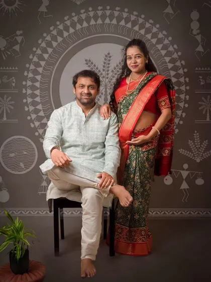 A full view of the Worli art inspired backdrop with the couple posing formally. This unique setup blends tradition with fine art photography.