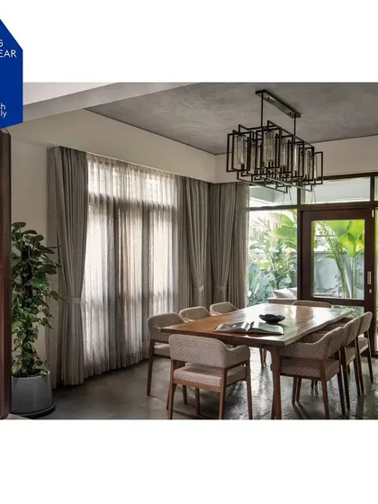 The dining space seamlessly extends into a side garden through large glass doors. This connection not only provides ample natural light but also allows for a fluid indoor-outdoor living experience, with elements like the traditional brass bell adding a layer of cultural context.