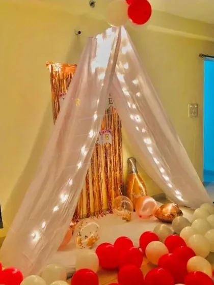 A simple and elegant canopy tent surprise. The sheer fabric tent is lit with fairy lights, with balloons on the floor, creating a dreamy and romantic hideaway.
