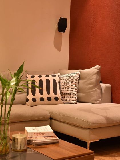 This living room combines chic elegance with coziness. A neutral L-shaped sofa provides a versatile foundation, while a rich, rust-colored accent wall adds warmth and depth.