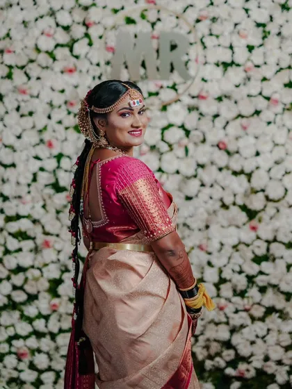 A classic bridal portrait against a wall of white flowers. The bride's smile and the beautiful details of her hair and saree are the highlights of this shot.