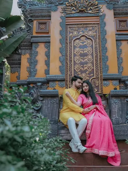 This pre-wedding photo has a majestic feel, with the couple seated before an ornate, temple-inspired backdrop. Their traditional outfits complete the grand picture.