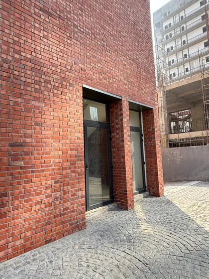 A ground-level detail of an exposed brick facade. This view highlights the precision in masonry and the clean integration of modern door frames, grounded by the texture of cobblestone paving.