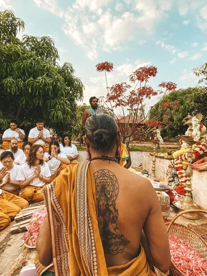 A group of students gathers for an outdoor puja. The image captures the devotion and focus of the participants against a beautiful natural backdrop.
