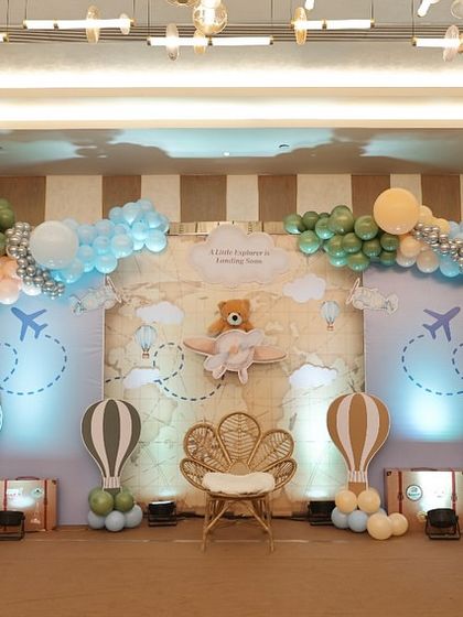 A full view of a travel-themed baby shower, with the message 'A Little Explorer is Landing Soon.' The decor includes hot air balloons, a world map, and vintage suitcases.