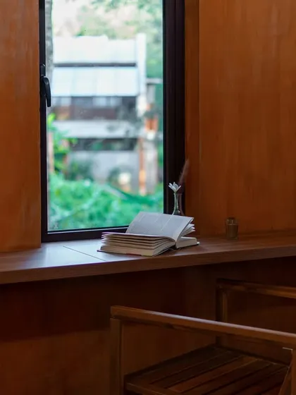 A quiet writing nook by a window, looking out onto the hills of Chikmagalur. This moody, atmospheric shot captures a moment of peace and tranquility, perfect for escaping the rigors of urban life.