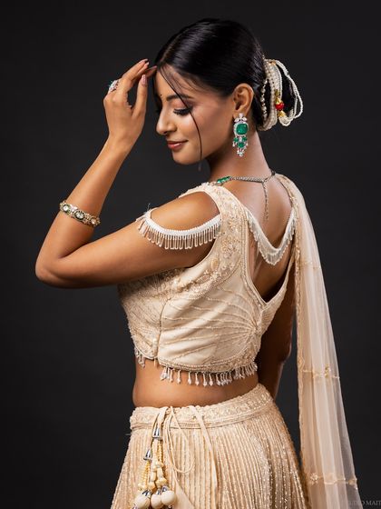 A side profile of the model in the cream lehenga, showing the elegant design of the blouse and the hairstyle.
