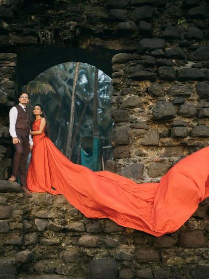 A dramatic pose at a stone ruin by the sea, with a vibrant orange gown creating a stunning visual contrast. This is a great example of a creative fort and beach pre-wedding shoot.