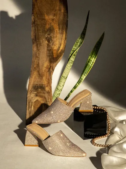 Creative product photography for women's block heels. The combination of wood, plants, and satin fabric creates a beautiful textural contrast that highlights the sparkling footwear.