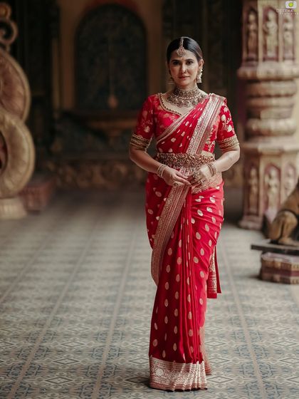 A grand, full-length portrait of me in the red Banarasi saree, standing in a heritage location.