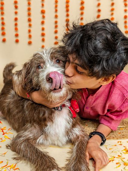 A boy gives his scruffy indie dog a big hug and a kiss during a festive Rakshabandhan-themed shoot. The dog's happy lick shows the mutual affection and the beautiful bond they share.