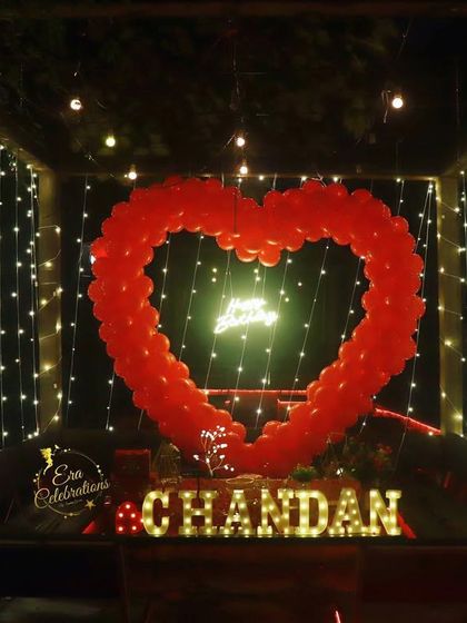 A romantic surprise setup featuring a red heart-shaped balloon arch inside a canopy of fairy lights. This is perfect for a truly memorable proposal or birthday.