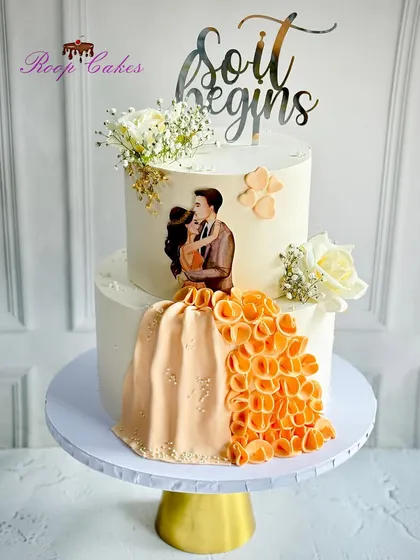 Sweet beginnings for a lifetime of love. This two-tier cake features an edible couple portrait with a flowing orange gown, creating a unique and personalized centerpiece for an engagement party.
