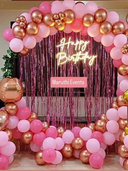 A glamorous first birthday in rose gold and pink. The circular balloon arch frames a shiny pink foil curtain, with a neon sign adding a modern touch.