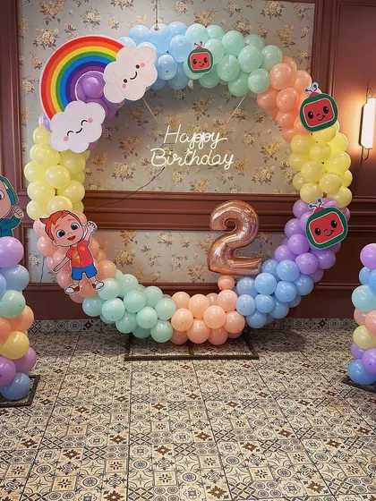 A bright and cheerful Cocomelon theme for a second birthday. This setup features a full ring balloon arch in pastel colors with character cutouts and a rainbow detail.