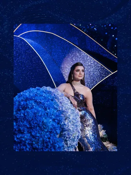 A stunning shot of the bride beside a large, spherical floral arrangement, all set against the deep, shimmering blue of the cosmic-themed decor.