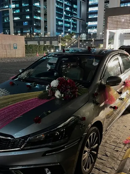 A simple yet elegant wedding car decoration using colorful drapes and a small floral bouquet on the bonnet.