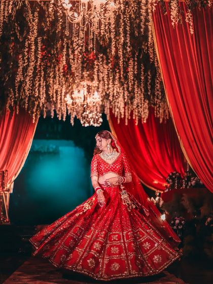 A bride twirls in her red lehenga under a canopy of flowers and red curtains, creating a vibrant and dynamic shot.
