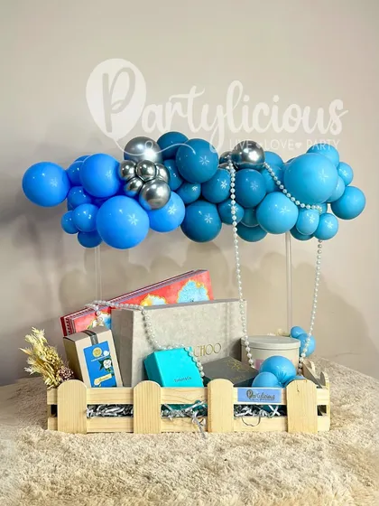 A gift hamper that floats! This creative arrangement features a wooden crate filled with gifts, with a blue balloon cloud seemingly lifting it into the air.