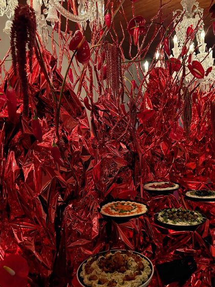 A modern and artistic food display, with pizzas presented amidst a landscape of shiny red metallic fabric and floral branches.