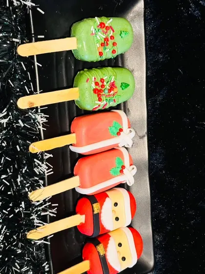 A collection of our Christmas-themed cakesicles. Designs include Santa's suit, festive holly, and green pops with sprinkles, perfect for holiday parties and gifting.